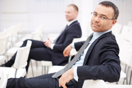 Confident businessman sitting in conference hall with his colleague on backgroundの写真素材