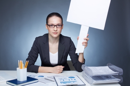 Portrait of serious businesswoman in eyeglasses holding blank card at workplaceの写真素材