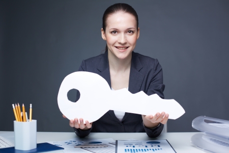 Portrait of young smiling female holding big paper key and looking at cameraの写真素材