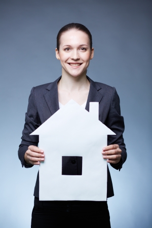 Portrait of young smiling female holding paper house and looking at cameraの写真素材