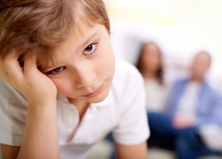 Portrait of sad boy looking at camera on background of his parentsの写真素材