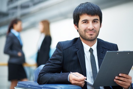 Portrait of confident male leader with clipboard looking at camera in working environmentの写真素材