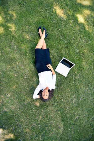 Above view of successful businesswoman lying on green grass with laptop near by  の写真素材