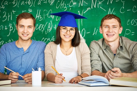 Portrait of three smart students looking at camera with chalkboard on backgroundの写真素材