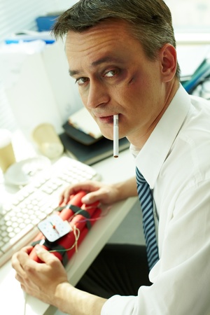 Portrait of businessman with bruised face and cigarette holding dynamite and looking at camera の写真素材