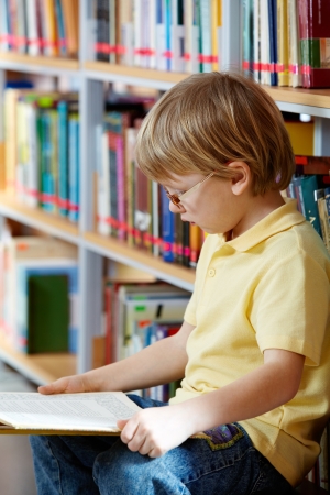 Portrait of clever boy reading book in libraryの写真素材
