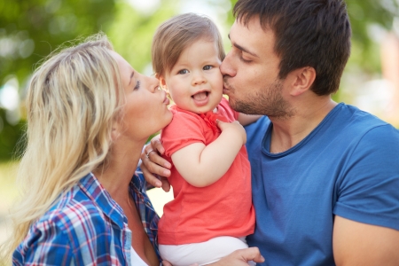 Photo of affectionate parents kissing their small daughterの写真素材