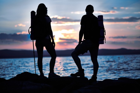 Rear view of couple of hikers standing by water in the eveningの写真素材