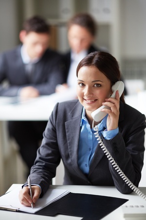 Portrait of smart businesswoman calling on the phone on background of working colleaguesの写真素材