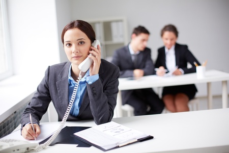 Portrait of smart businesswoman calling on the phone on background of working colleaguesの写真素材