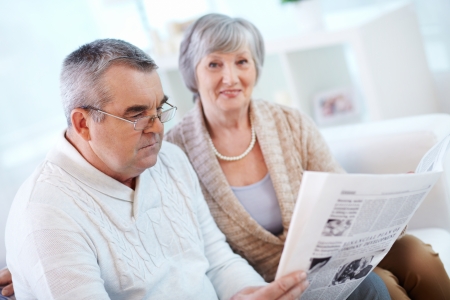 Portrait of mature man reading newspaper at home with his wife near byの写真素材