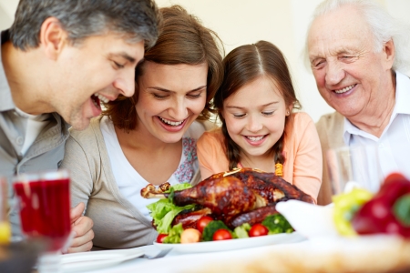 Portrait of happy family sitting at festive table and looking at roasted turkeyの写真素材