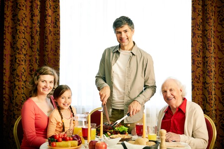 Portrait of happy family by festive table looking at camera on holiday evening 