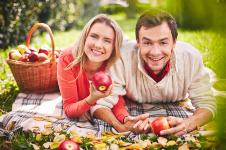 Happy young couple with ripe apples looking at camera in parkの写真素材