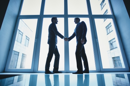 Silhouettes of two successful businessmen handshaking after striking dealの写真素材