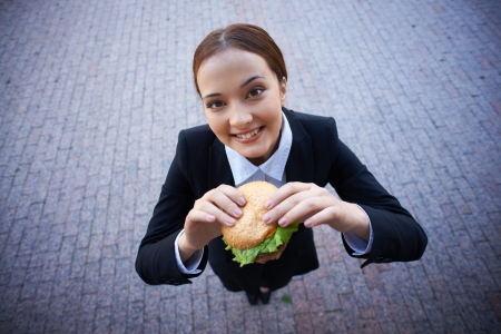 Businesswoman with sandwich looking at camera outsideの写真素材