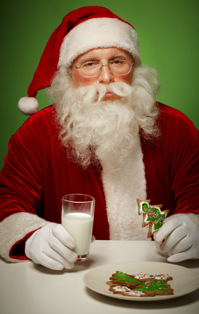 Photo of Santa Claus in eyeglasses eating gingerbread with milkの写真素材