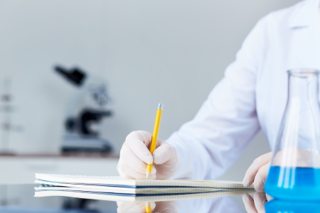 Hand of chemist with pencil writing down observations in laboratoryの写真素材