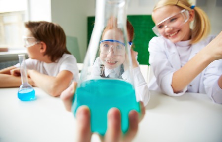 Happy schoolgirl holding tube with chemical liquid and looking at camera through itの写真素材