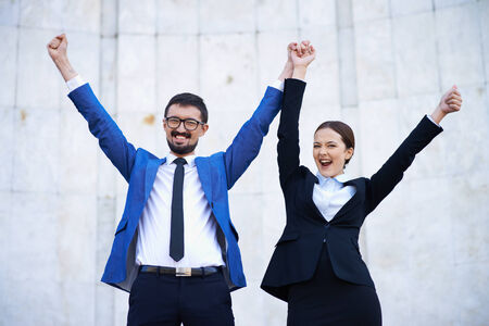 Happy businessman and businesswoman with raised arms looking at cameraの写真素材