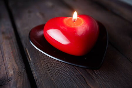 Image of red heart shaped candle burning on wooden の写真素材