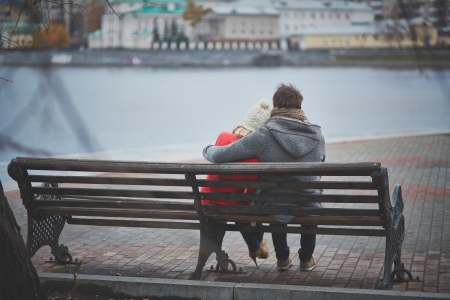 Back view of affectionate couple sitting on the bench and looking at riverの写真素材