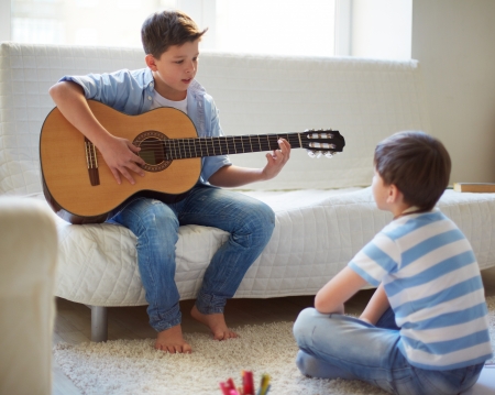 Portrait of handsome boy playing the guitar with his brother near byの写真素材