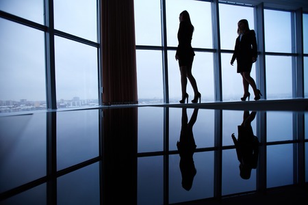 Silhouettes of two businesswomen standing against window in officeの写真素材