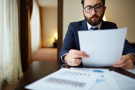 Serious businessman in suit reading document in officeの写真素材