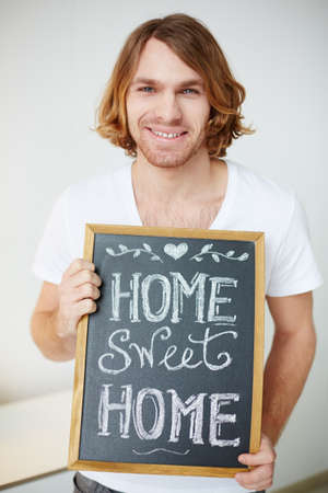 Photo of young man holding small board with message about homeの写真素材