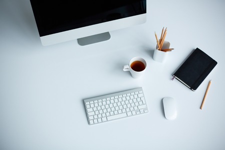 Image of cup of tea, monitor, keypad, pencils in glass, notebook and computer mouse on deskの写真素材