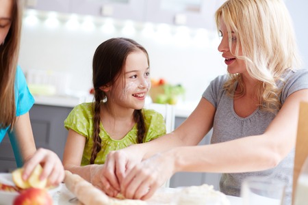Portrait of happy girl helping her mother to cook pastryの写真素材