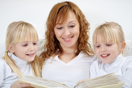 Portrait of mother reading tales to daughters in bedの写真素材