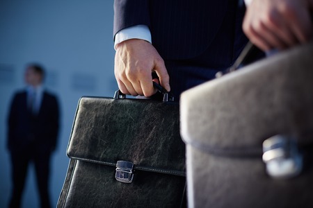 Cropped image of business partners carrying briefcases on the foreground while their colleague standing on the background