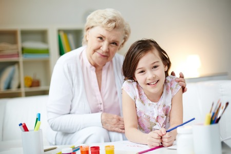 Portrait of happy girl and her grandmother sitting at homeの写真素材