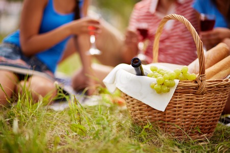 Basket with bottle, bread and grapes on background of cheering friendsの写真素材