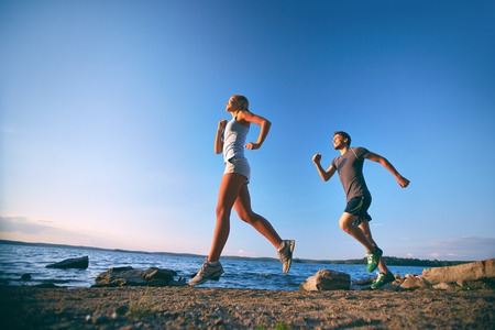 Photo of young couple running on the coastlineの写真素材