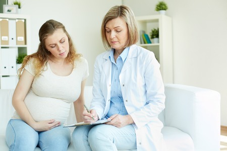 Young pregnant woman listening to prescription of doctor after regular examination at hospitalの写真素材