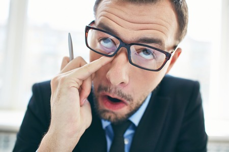 Face of funny businessman in eyeglasses rubbing eyeの写真素材