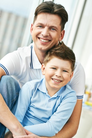 Photo of happy man embracing his son and both looking at cameraの写真素材