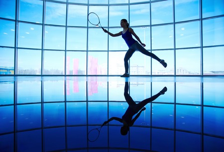 Young female playing tennis in gym on background of windowの写真素材