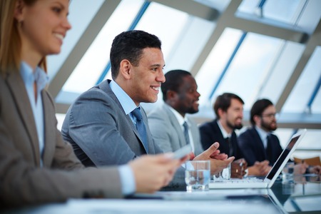 Row of business people listening to presentation at seminar with focus on elegant young man
