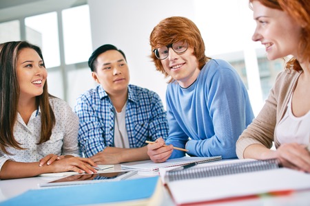 Company of smart groupmates sitting at lesson, guy in eyeglasses looking at cameraの写真素材