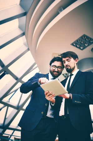 Image of young businessman holding touchpad while listening to explanation of his colleague at meetingの写真素材