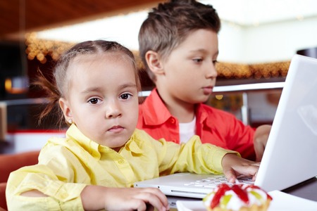 Portrait of cute children typing on laptop, little girl looking at camera