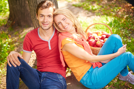 Happy young couple sitting in park and looking at cameraの写真素材