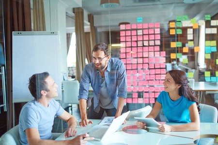 Group of three successful business partners in casual communicating at meeting in office