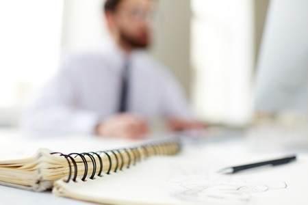 Spiral notepad with pen at workplace, focus on binderの写真素材