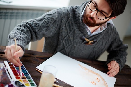 Young man in sweater drawing female portrait with water-colorsの写真素材