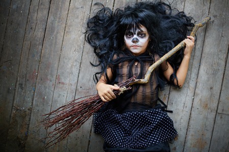 Portrait of cute Halloween girl with broom looking at camera